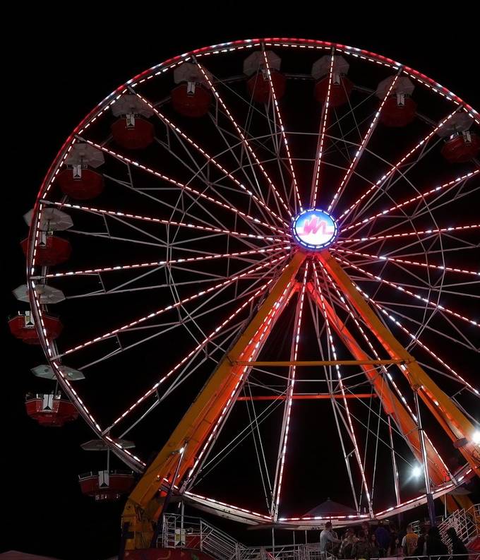 A Ferris wheel outlined in red and white lights against the night sky at a fair. Photograph by Digital Life Concepts.