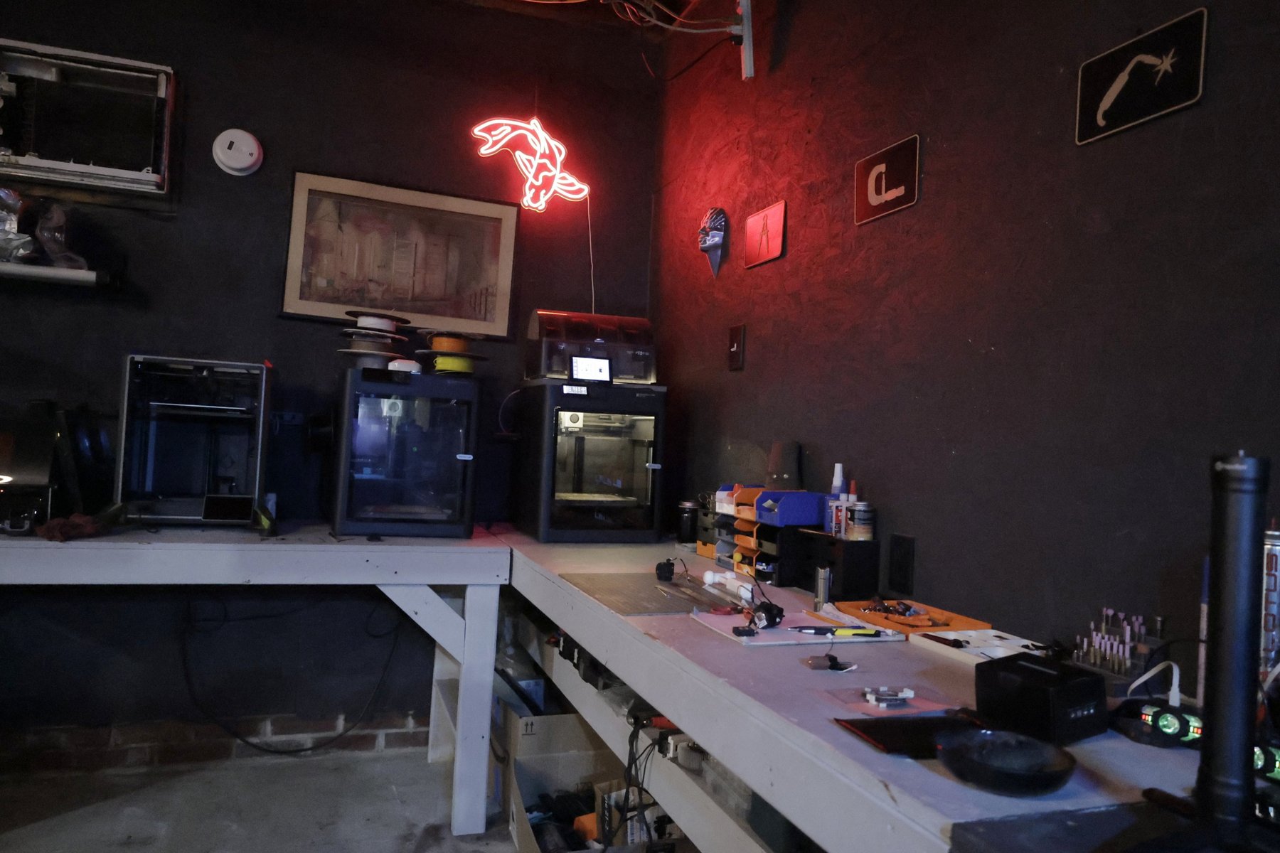 The TacticalTech3D workbench with parts, tools, and storage bins, the printer bench behind it.